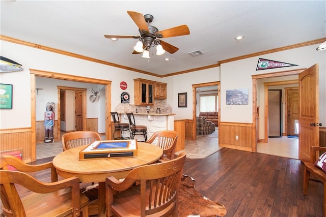 dining area with ceiling fan, crown molding, light hardwood / wood-style floors, and wooden walls