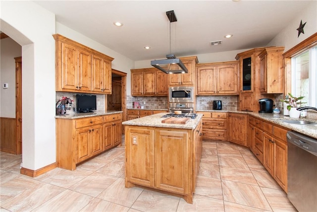 kitchen featuring light stone countertops, appliances with stainless steel finishes, sink, pendant lighting, and a center island