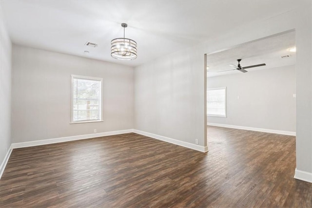 empty room with ceiling fan with notable chandelier, a healthy amount of sunlight, and dark hardwood / wood-style flooring