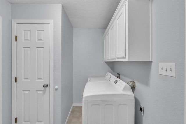 laundry area featuring cabinets, light tile patterned floors, a textured ceiling, and washing machine and clothes dryer