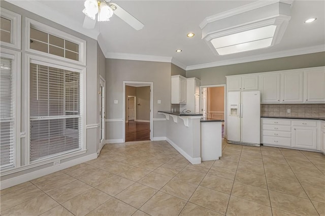 kitchen with crown molding, kitchen peninsula, decorative backsplash, white fridge with ice dispenser, and white cabinetry