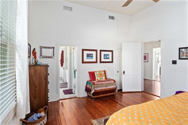 bedroom with ensuite bath, ceiling fan, hardwood / wood-style floors, and a high ceiling