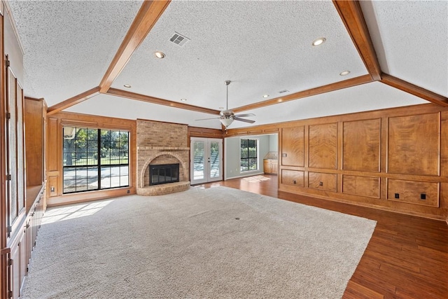 unfurnished living room featuring a textured ceiling, ceiling fan, dark wood-type flooring, a fireplace, and vaulted ceiling with beams