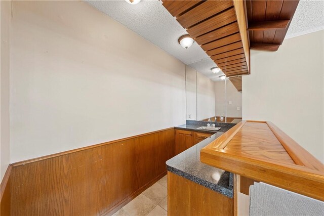 bar with sink, wood walls, a textured ceiling, light tile patterned flooring, and ornamental molding