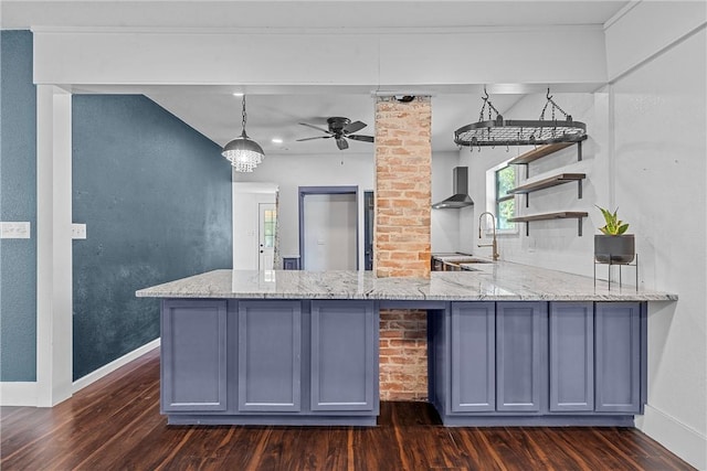 kitchen featuring kitchen peninsula, light stone counters, dark wood-type flooring, wall chimney range hood, and pendant lighting