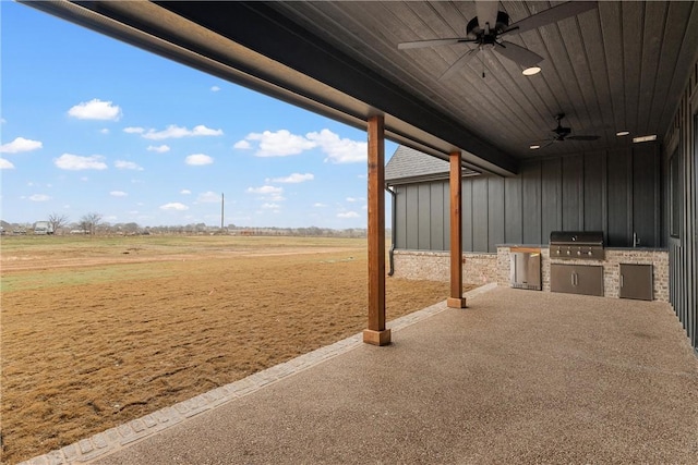 view of patio featuring grilling area, an outdoor kitchen, a rural view, and ceiling fan