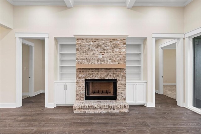 unfurnished living room with beamed ceiling, a brick fireplace, dark wood-type flooring, and built in shelves