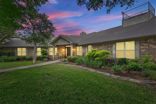 ranch-style house with a balcony and a lawn