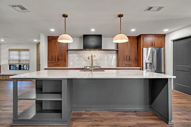 kitchen featuring dark wood-style floors, visible vents, stainless steel fridge, and a large island with sink