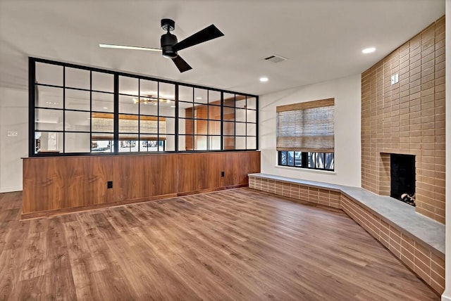 unfurnished living room with visible vents, a brick fireplace, ceiling fan, recessed lighting, and wood finished floors