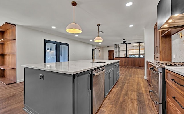 kitchen with a center island with sink, gray cabinets, appliances with stainless steel finishes, wall chimney exhaust hood, and a sink