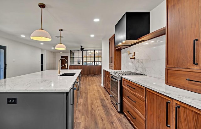 kitchen featuring an island with sink, a sink, gas stove, brown cabinetry, and decorative backsplash