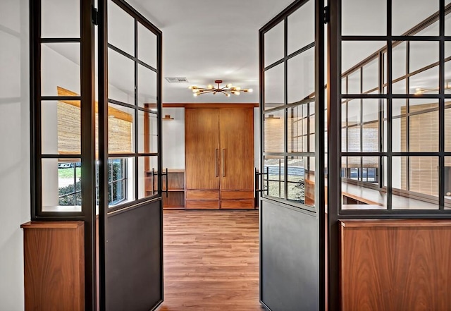 doorway to outside with a chandelier, visible vents, plenty of natural light, and wood finished floors