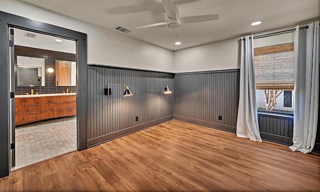 empty room featuring visible vents, light wood-type flooring, ceiling fan, and a wainscoted wall