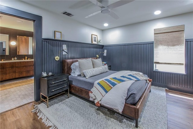 bedroom featuring wood finished floors, visible vents, a wainscoted wall, ceiling fan, and connected bathroom