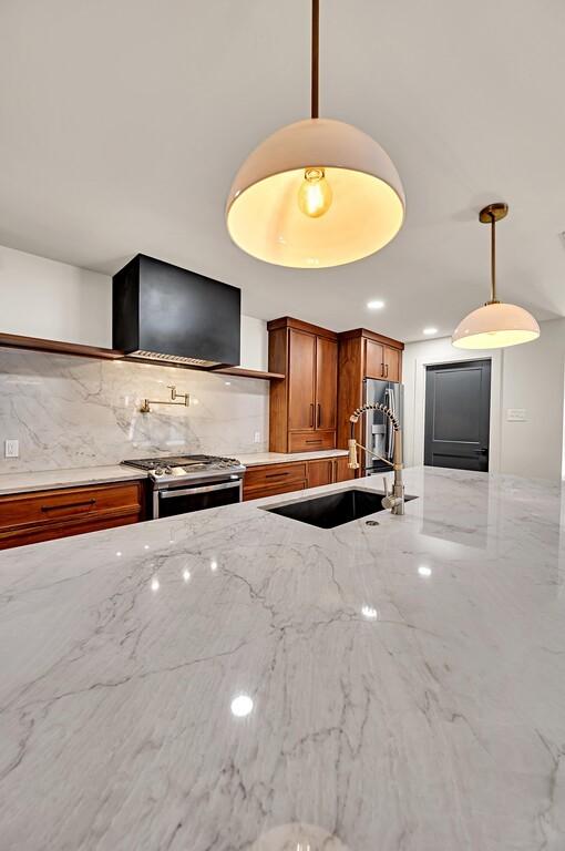 kitchen with light stone countertops, brown cabinetry, a sink, hanging light fixtures, and appliances with stainless steel finishes