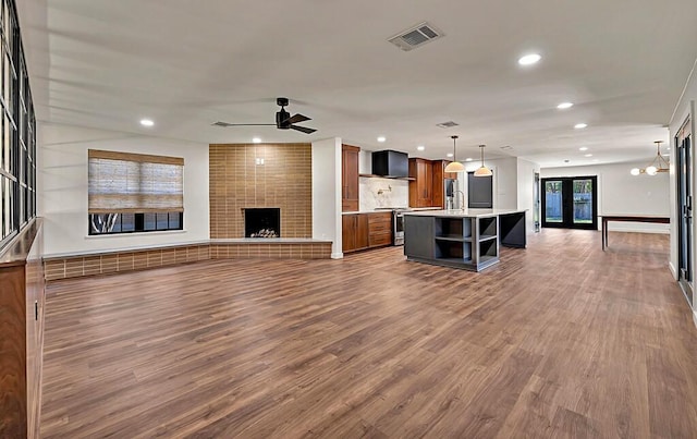 unfurnished living room with visible vents, a ceiling fan, wood finished floors, recessed lighting, and a brick fireplace