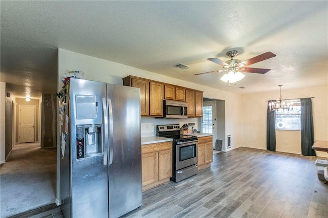 kitchen with a textured ceiling, decorative light fixtures, appliances with stainless steel finishes, ceiling fan with notable chandelier, and light wood-type flooring