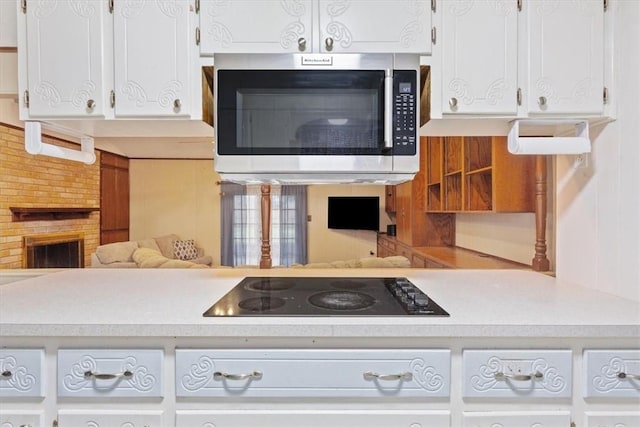 kitchen featuring black electric cooktop, a brick fireplace, and white cabinetry