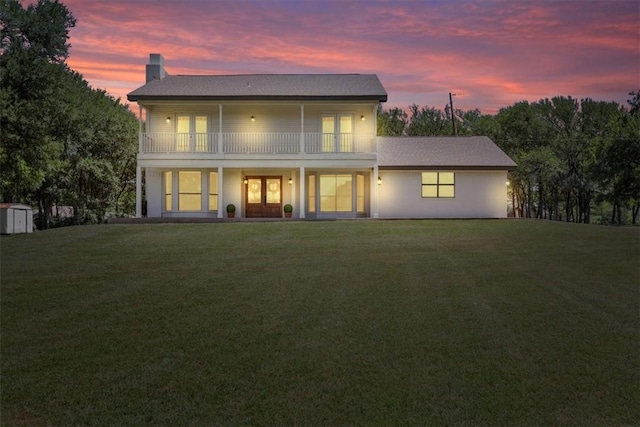 back house at dusk with french doors, a yard, and a balcony