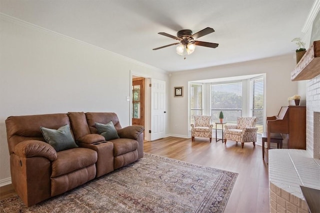 living room featuring ceiling fan, hardwood / wood-style floors, ornamental molding, and a brick fireplace