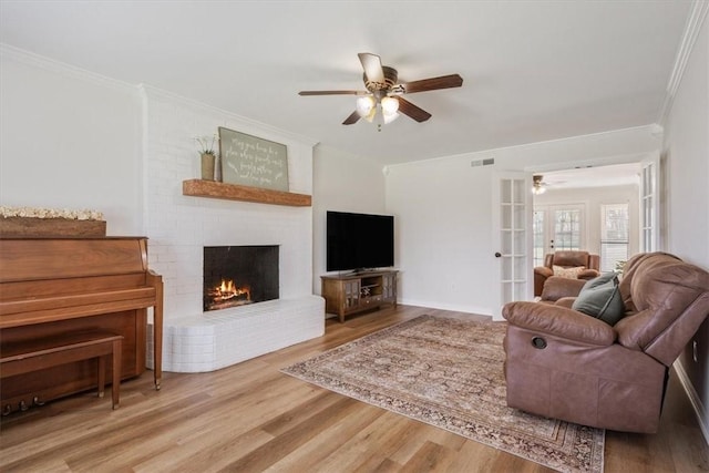 living room featuring ceiling fan, french doors, a brick fireplace, crown molding, and hardwood / wood-style flooring