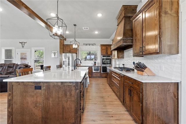 kitchen with custom exhaust hood, a spacious island, light wood-type flooring, decorative light fixtures, and stainless steel appliances