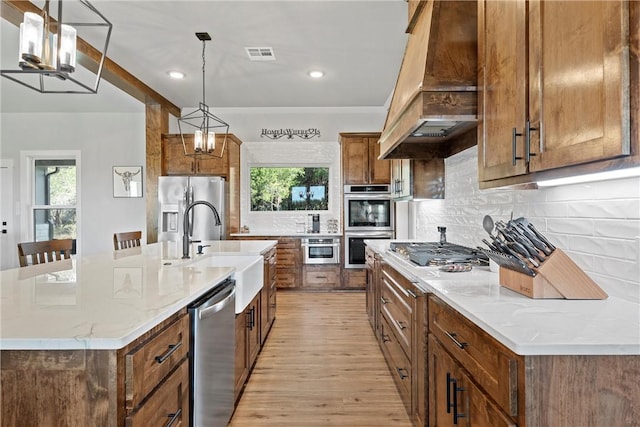 kitchen featuring sink, hanging light fixtures, appliances with stainless steel finishes, light hardwood / wood-style floors, and custom range hood