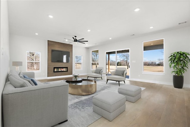 living room featuring ceiling fan, light wood-type flooring, and a fireplace