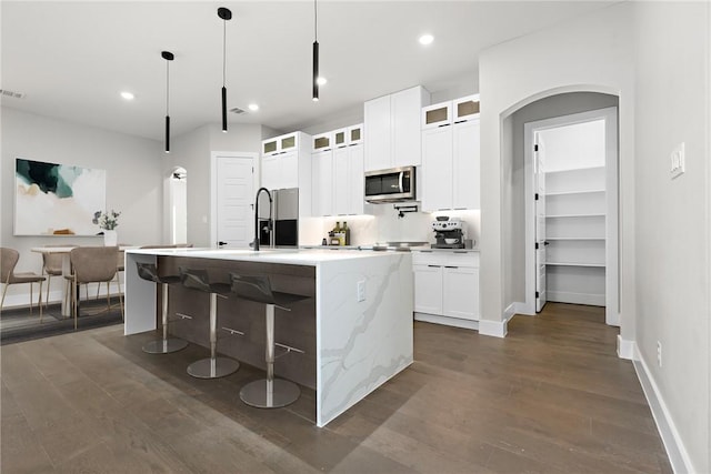 kitchen with a kitchen island with sink, hanging light fixtures, white cabinetry, dark hardwood / wood-style floors, and light stone counters