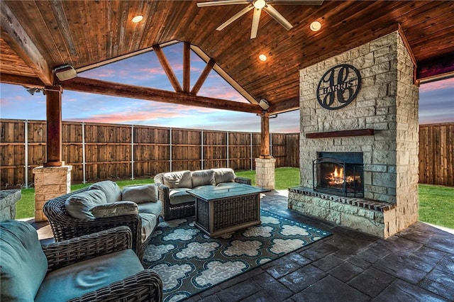 patio terrace at dusk featuring an outdoor living space with a fireplace, ceiling fan, and a gazebo