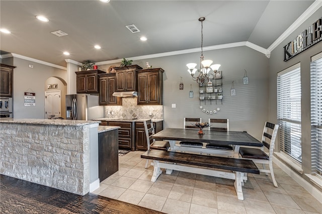 kitchen with dark brown cabinetry, stainless steel appliances, a notable chandelier, vaulted ceiling, and ornamental molding