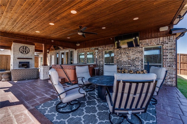 view of patio / terrace featuring an outdoor stone fireplace, a hot tub, and ceiling fan