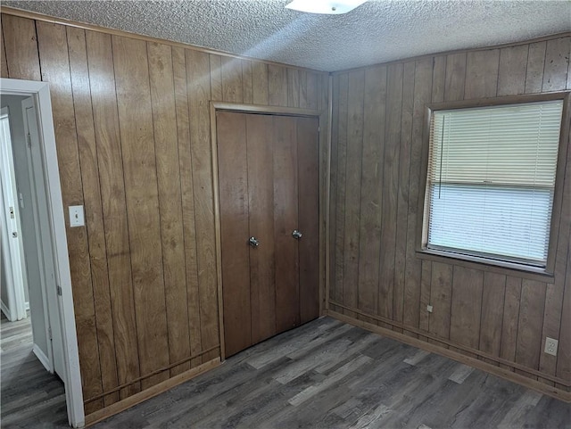 unfurnished bedroom with a textured ceiling, wooden walls, a closet, and dark hardwood / wood-style floors