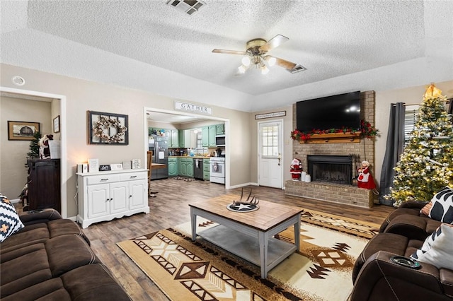 living room with ceiling fan, a fireplace, a textured ceiling, and light wood-type flooring