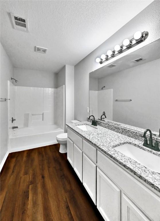 full bathroom with vanity, a textured ceiling, hardwood / wood-style flooring, washtub / shower combination, and toilet