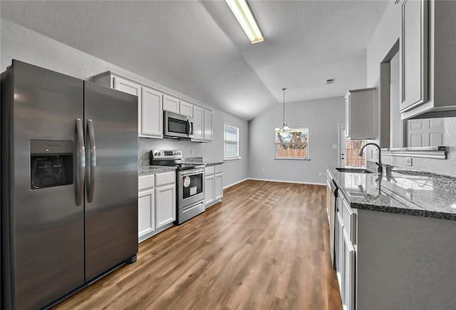 kitchen featuring dark stone counters, stainless steel appliances, vaulted ceiling, sink, and pendant lighting