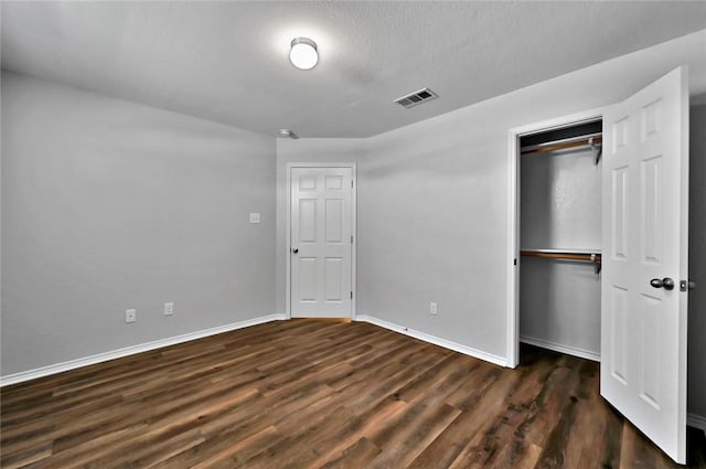 unfurnished bedroom featuring a textured ceiling, dark hardwood / wood-style floors, and a closet