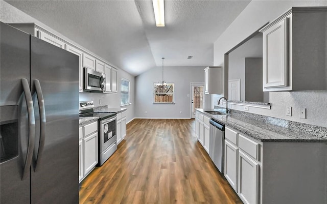 kitchen featuring sink, stainless steel appliances, dark stone countertops, pendant lighting, and vaulted ceiling