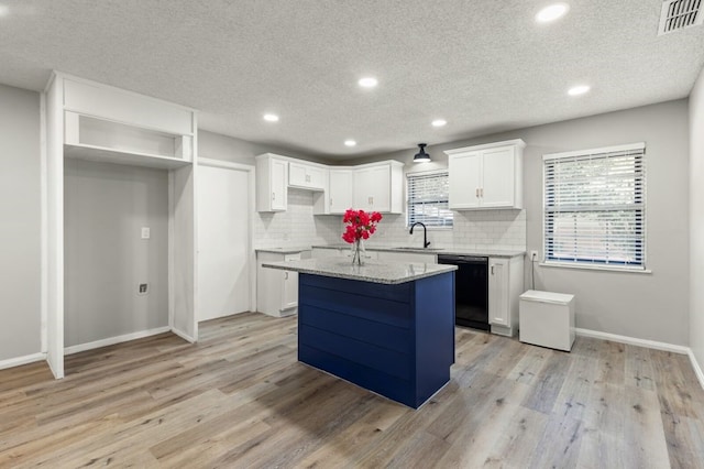 kitchen with dishwasher, light hardwood / wood-style flooring, a kitchen island, light stone counters, and white cabinetry