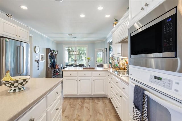 kitchen with appliances with stainless steel finishes, light countertops, a peninsula, and ornamental molding