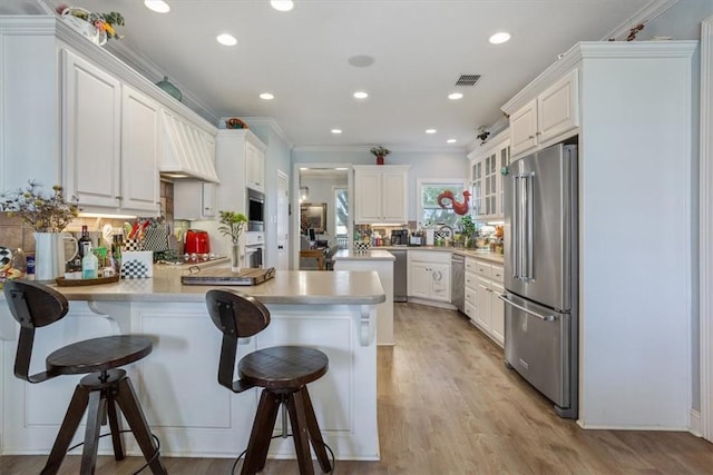 kitchen with a peninsula, ornamental molding, light countertops, appliances with stainless steel finishes, and a kitchen bar