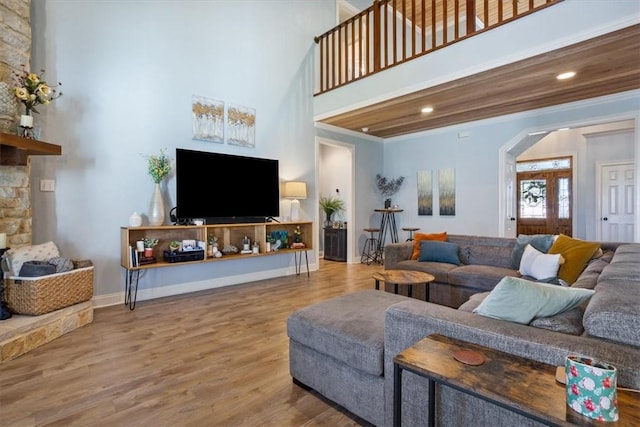 living area with ornamental molding, wood finished floors, arched walkways, a high ceiling, and baseboards