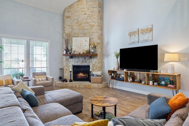 living room with a stone fireplace, crown molding, a high ceiling, and wood finished floors