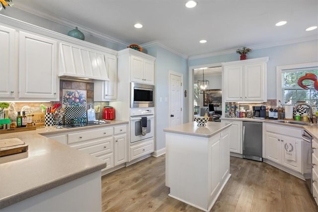 kitchen with a sink, light wood-type flooring, appliances with stainless steel finishes, and ornamental molding