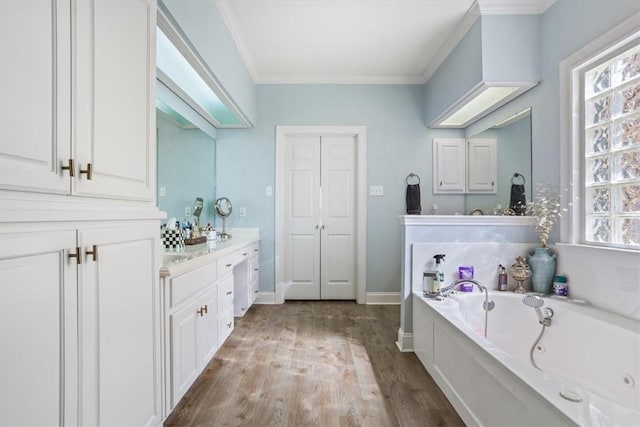 bathroom featuring vanity, wood finished floors, baseboards, crown molding, and a jetted tub