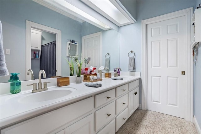 full bath featuring a sink, speckled floor, a skylight, and double vanity