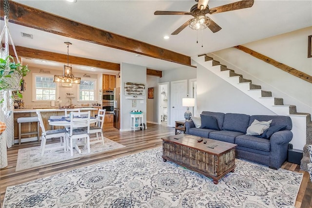 living room with beam ceiling, ceiling fan with notable chandelier, and light hardwood / wood-style floors