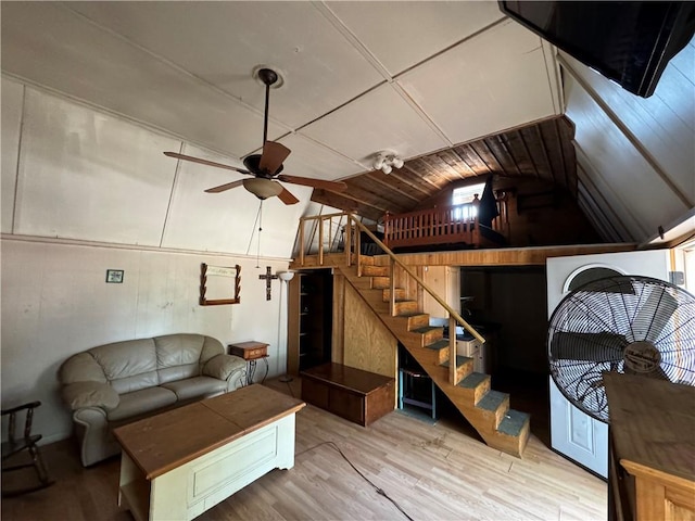 living room featuring light hardwood / wood-style floors, vaulted ceiling, ceiling fan, and wood walls