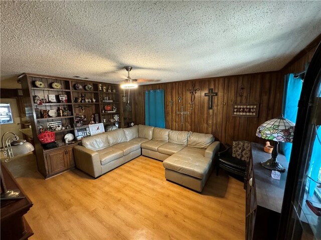 living room with ceiling fan, a textured ceiling, wooden walls, and light hardwood / wood-style flooring